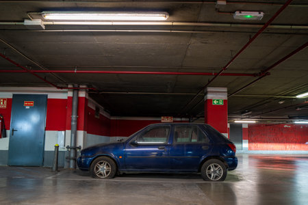 Blue car with visibly deflated tires parked near red walls in a concrete parking structureの写真素材