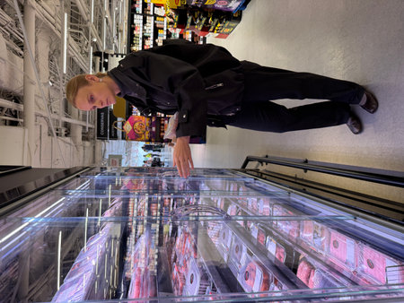 Woman in black outfit selects packaged meat from refrigerated section with focused expression