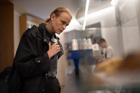 Woman holding a smartphone while observing pastries behind a glass display in a bakery setting