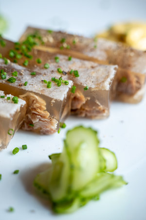 Close-up view of a gourmet aspic dish garnished with fresh chives and served with sliced cucumber on...