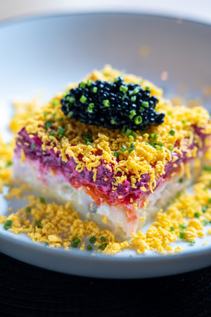 Close-up of a vibrant layered salad topped with black caviar and garnished with chives and egg...