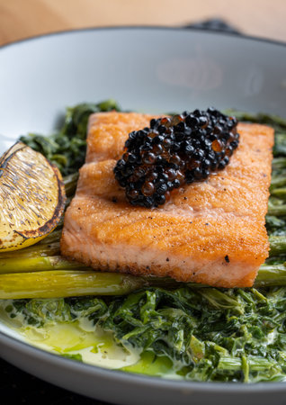 Deliciously plated gourmet salmon topped with black caviar served on greens and grilled lemon slice on the side.の写真素材