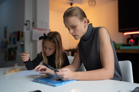 Mother and daughter sit at the table as they work together on homework in a cozy home setting