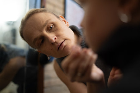 Woman with short hair intensely examines her reflection in a mirror with focused expression