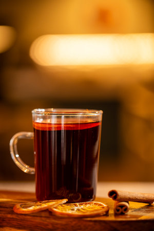 A glass of mulled wine with orange slices and cinnamon sticks on a wooden table in warm lightingの写真素材