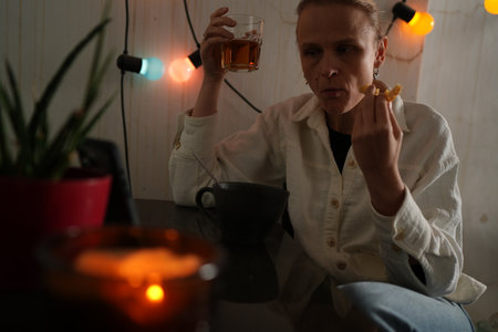 Woman with light shirt eating and drinking at a dark table with warm lighting and plants around