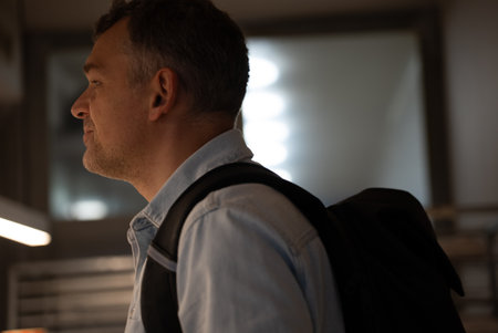 Side view of man with backpack standing indoors in bakery looking at the counter