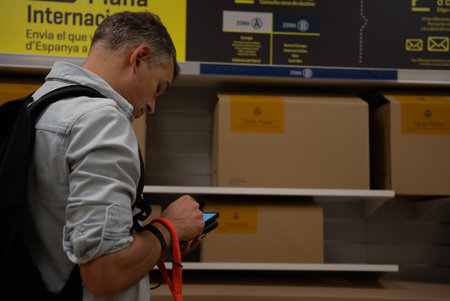 Man in casual outfit using smartphone near international parcels section in postal office