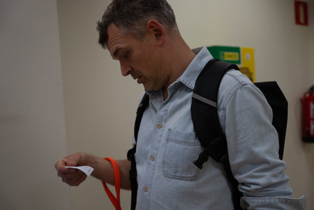 Casual man with backpack looking at printed receipt while standing indoors at post office