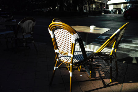 Wicker chairs and table at outdoor street cafe lit by low morning sunlight and shadows