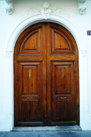 Symmetrical arched wooden double door framed by ornate white stucco detailing on exterior wall