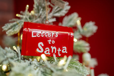 Red mailbox labeled Letters to Santa hanging on snowy Christmas tree with warm festive lightsの写真素材