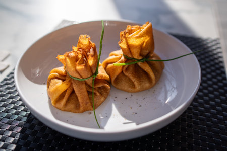 Close up of blini shaped like money bags tied with green chive on white plate for Maslenitsa...