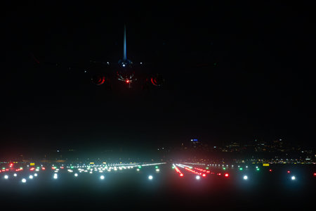 Commercial jet landing at night with bright runway guidance lights and city glowの写真素材