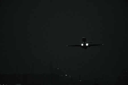 Monochrome view of a commercial jet aircraft approaching the runway with illuminated headlights in...