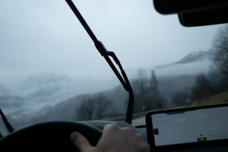 Car dashboard and windshield wipers active while navigating a mountain route in heavy fog and rainy...