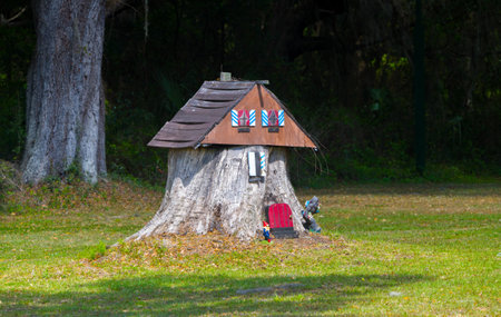 old tree stump turned into a garden fairy gnome house in the middle of Grass field with tiny bigfootの写真素材