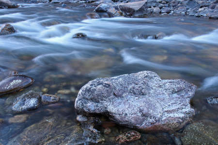 Icy cold water flows over the rounded rocks of the Poudre River in Coloradoの写真素材