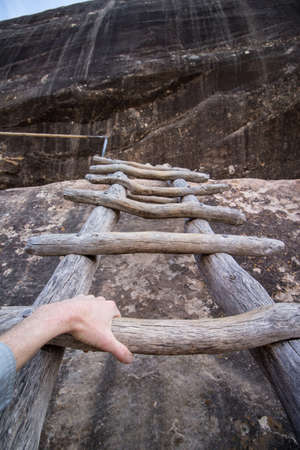 First person pov photo from a hiker climbing a wooden ladder up a cliff.