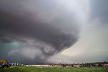 A huge supercell storm with a ground scraping wall cloud and lightning bolt fills the sky.