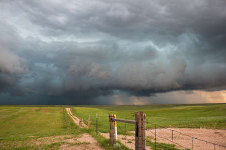 A dark storm looms on the horizon at the end of a dirt road in the countryside.の写真素材