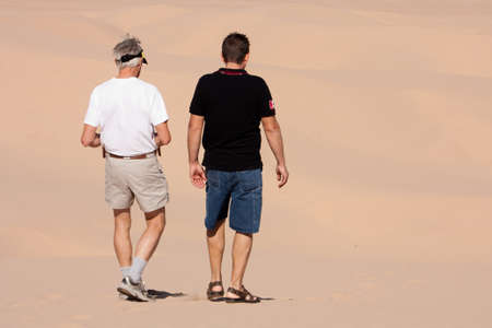 Two men engaged in conversation as they walk away from the camera into the sandy desert dunes backgroundの写真素材