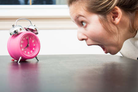 Close up as a young woman gapes at a pink alam clock in shocked panicの写真素材