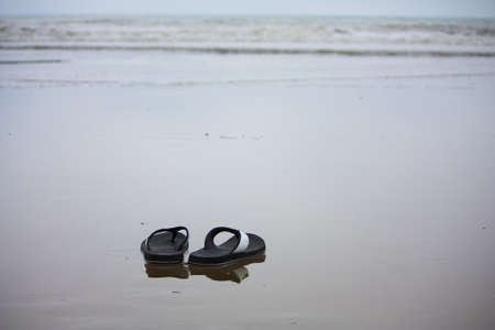 Sandals sitting on the secluded sand beach at Jama Ecuador at sunset   The waves flow out slowly leaving a glassy reflective surface on the flat sand の写真素材