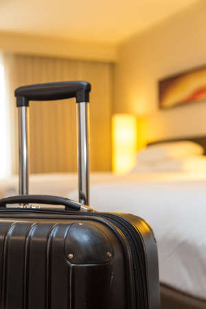 a hard sided black suitcase in focus, with a hotel room in the backgroundの写真素材