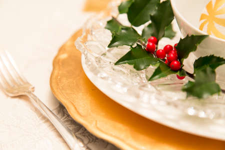 Layers of golden and vintage tableware with fresh holly in a classic Christmas table set for dinnerの写真素材