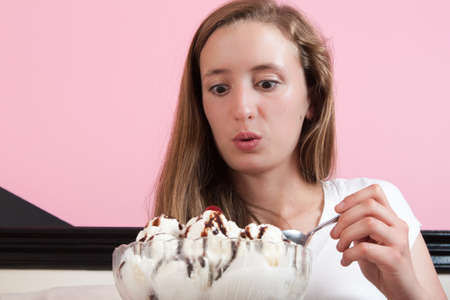 close up of an excited  teen aged woman as she digs into a huge ice cream sundae