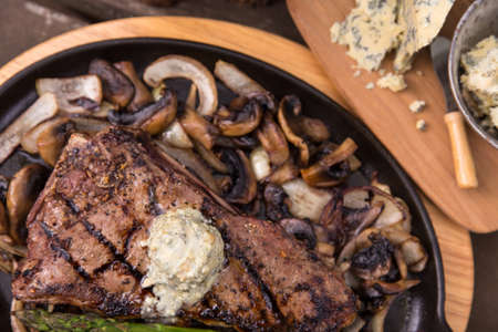 delicious grilled steak shown from above on a cast iron skillet surrounded by fried onions and mushrooms, and topped with blue cheese steak butterの写真素材