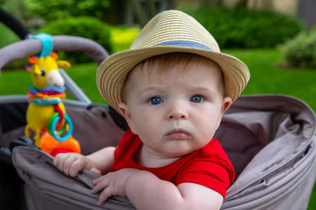 cute baby boy wearing a hat sitting looking out the side of his stoller