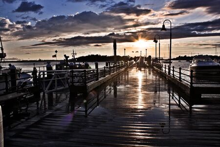 Fishing pier at sunset. This wooden pier reflecting the water puddles after the rain as the clouds break for a glowing sunsetの写真素材