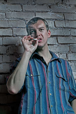 dramatic view of a man with a cigarette against the brick wallの写真素材