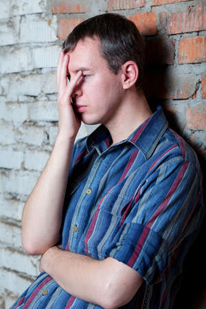 an upset man with a hand by his face reclined against the brick wallの写真素材