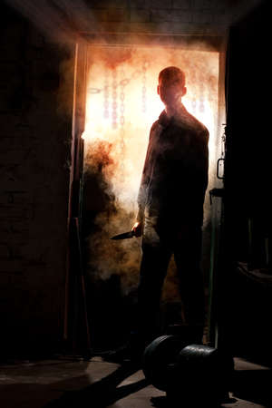 Silhouette of killer, standing with knife in his hand against smokeの写真素材