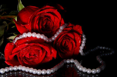 Red roses and white necklace lies on the reflective surface. The background is black.の写真素材