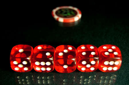 Five red dice on a green poker table. In the background lies poker chips.の写真素材