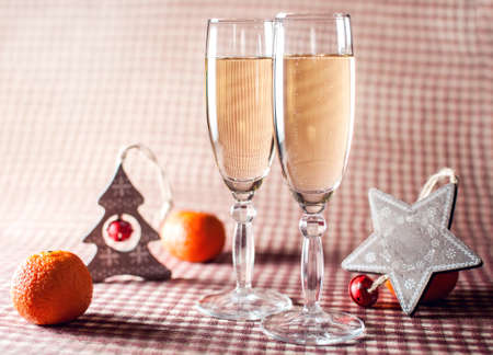 Image of two wineglasses of champagne, decorative wooden star and tree and mandarins on the red checkered background. Rustic style.の写真素材