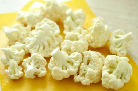 Chopped pieces of cauliflower on yellow cutting board. Prepared raw ingredients for cooking.の写真素材