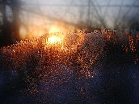 Frost ice crystals and water drops on window glass on the background of rising sun. Close up, contrast vivid colors.の写真素材