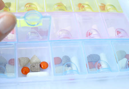 Closeup view of open transparent plastic pill organizer with drugs inside for a weekly dosage. Selective focus.の写真素材