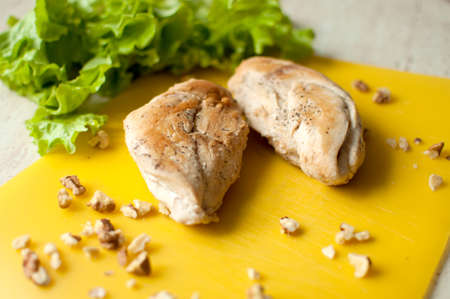 Ruddy chicken breasts with leaf salad and crushed walnut on yellow cutting board. Ingredients for salad preparation.の写真素材