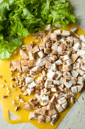 Chopped ruddy chicken breasts with leaf salad and crushed walnut on yellow cutting board. Ingredients for salad preparation. Top view.の写真素材