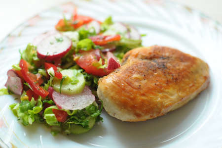 Baked chicken breast with vegetable salad on a white plate close up. Selective focus.の写真素材