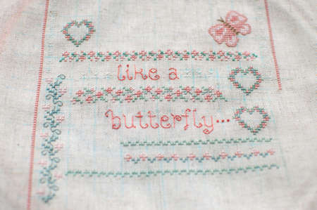 Cross-stitch embroidery on linen. Sampler with floral patterns, hearts and butterfly. Close up. Selective focus.の写真素材