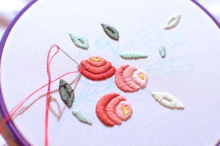 Embroidery with floral motif framed in a hoop. Work in process. Close up, soft selective focus.