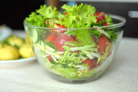fresh vegetable salad with tomato, cucumber and salad frisee in glass bowl. Process of cooking. Close up, selective focus.の写真素材