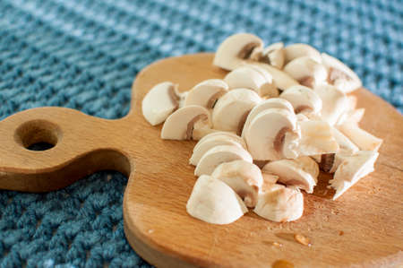 The process of cutting champignon mushrooms on a wooden cutting board on blue fabric knitted background close-upの写真素材